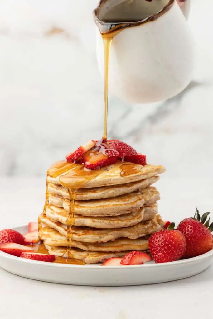 a stack of strawberry pancakes with maple syrup being poured over them