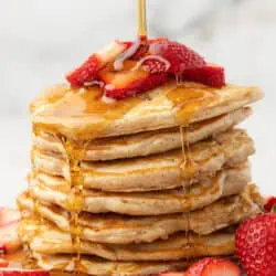 stack of strawberry pancakes with maple syrup poured over them