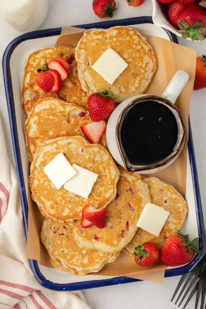 sheet pan with strawberry pancakes topped with butter and a dish of syrup