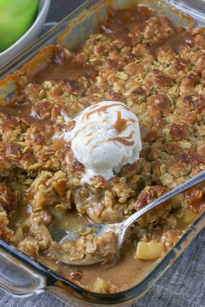 baking dish of apple caramel crisp topped with a scoop of vanilla ice cream