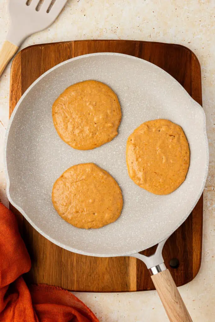 three pumpkin pancakes cooking in a skillet