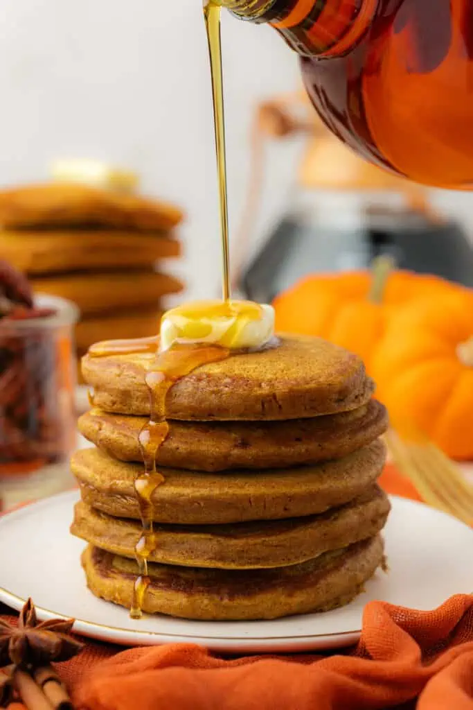 maple syrup drizzled over a stack of pumpkin pancakes