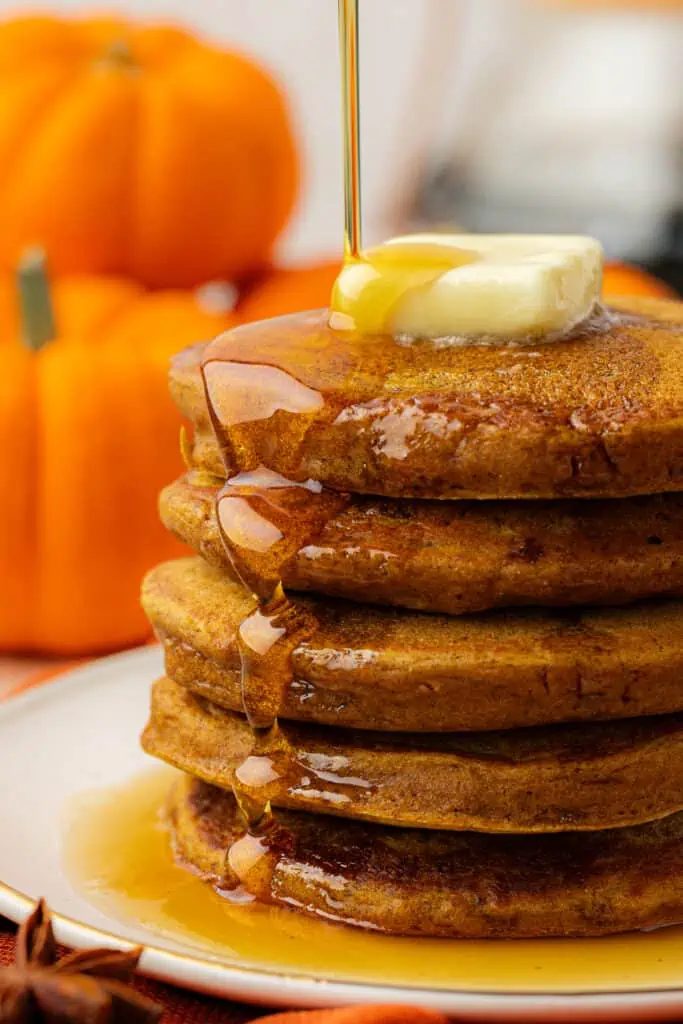 stack of pumpkin pancakes being drizzled with maple syrup