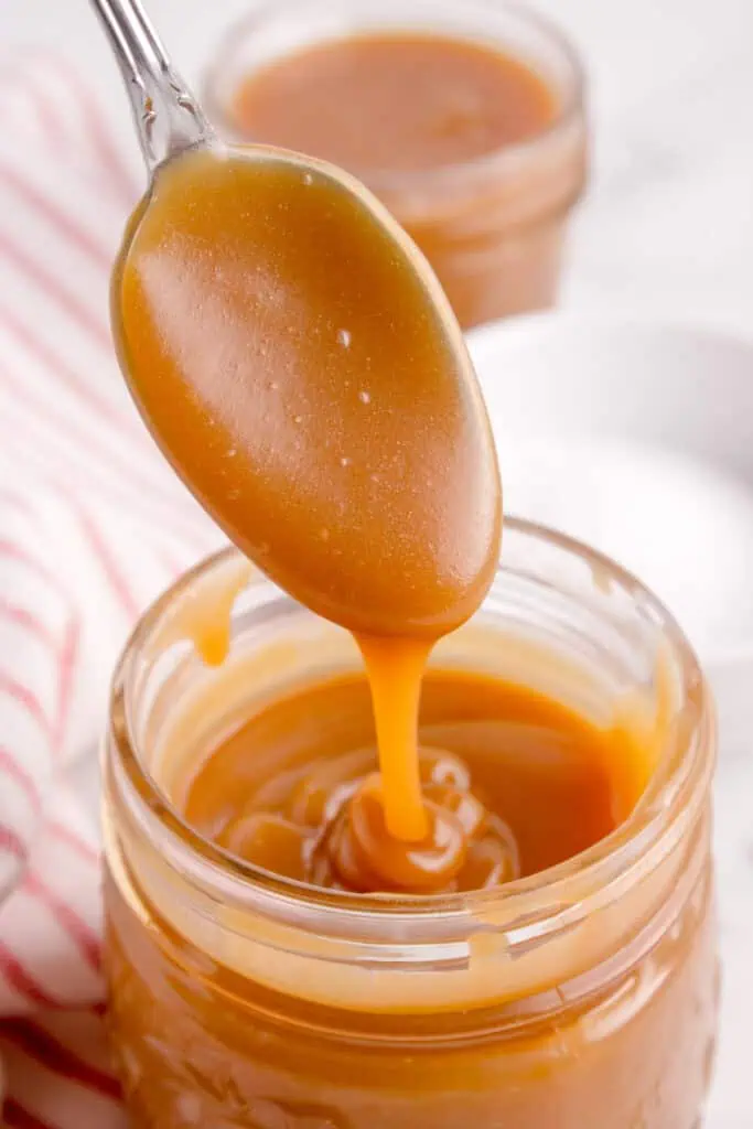spoon dipping into a jar of caramel sauce
