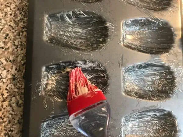 Learn how to make French Madeleines in this step by step baking photo tutorial! silicone brush brushing butter onto a madeleine pan