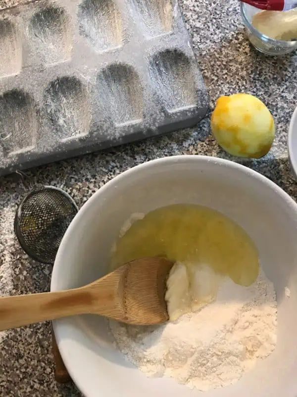 Learn how to make French Madeleines in this step by step baking photo tutorial! bowl of egg whites being stirred into dry ingredients