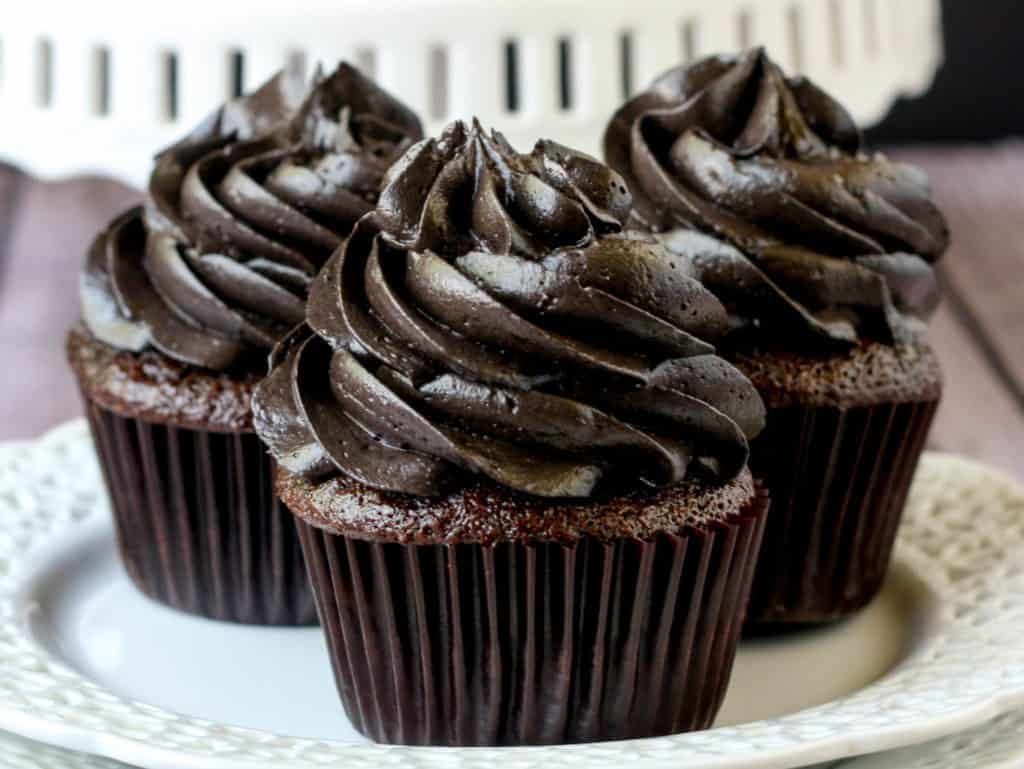 Three cupcakes with black icing on a white plate