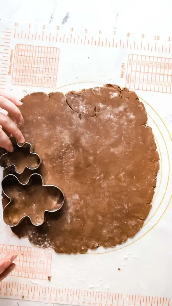 gingerbread cookie dough being cut out with cookie cutters