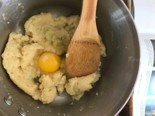 egg added to choux pastry in a pot