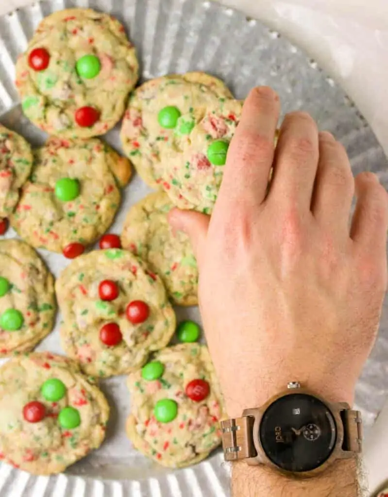 hand wearing a watch grabbing a M&M Christmas cookie off a platter of cookies