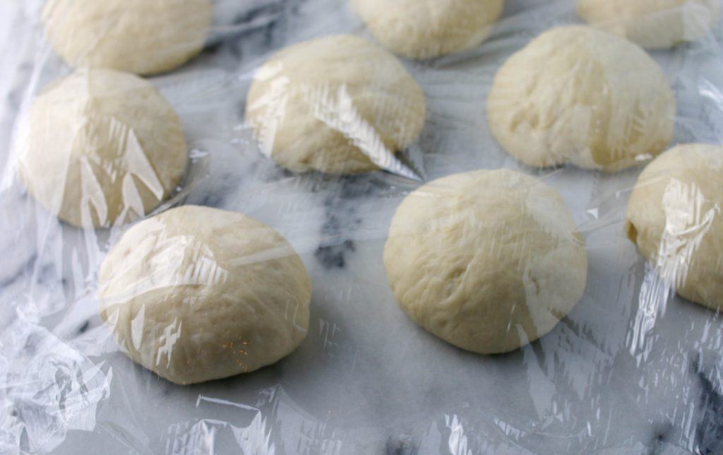 bagel dough balls resting under plastic wrap