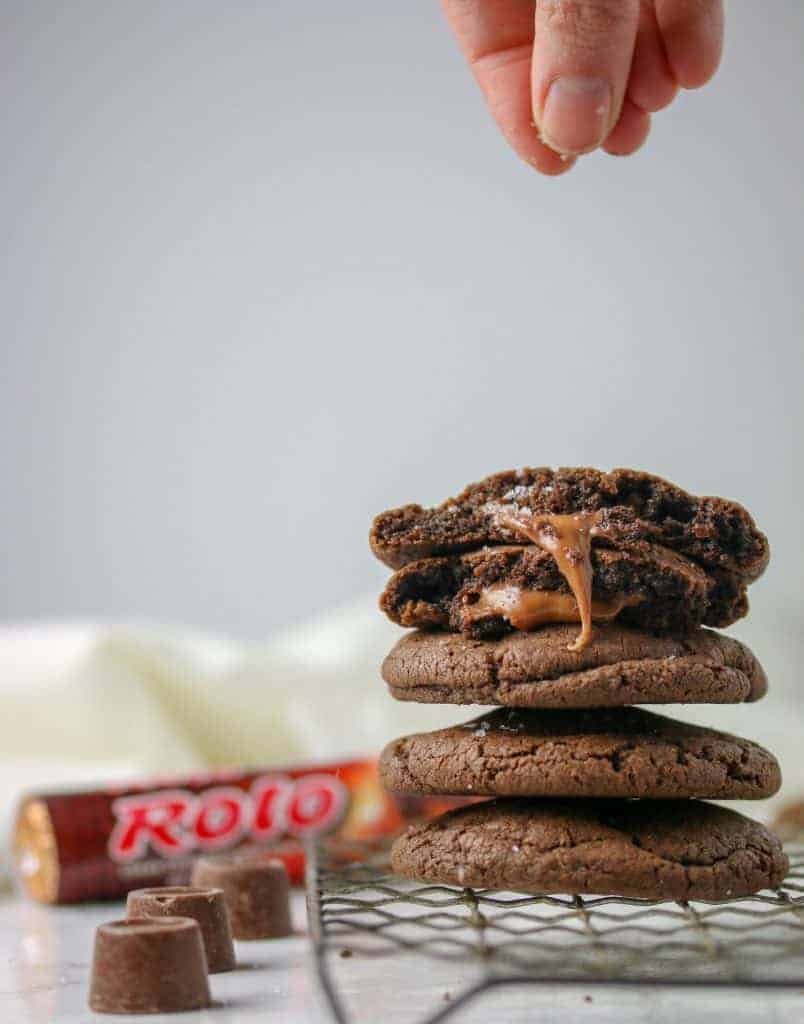 hand sprinkling salt on top of stack of five chocolate rolo cookies on a cooling rack