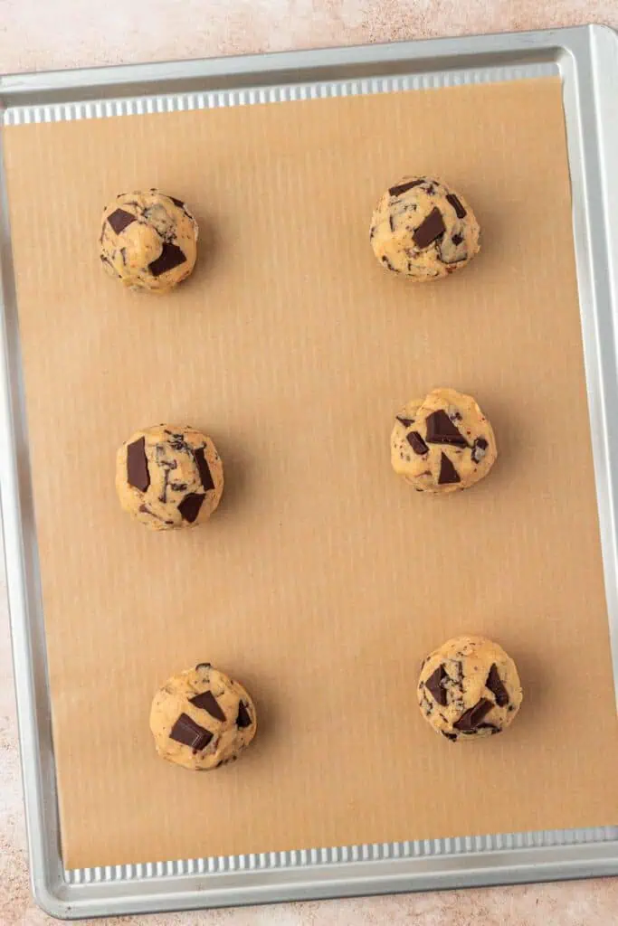 six chocolate chip cookie dough balls on a cookie sheet