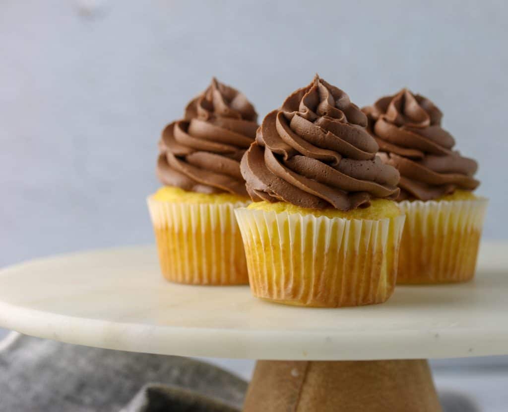 three cupcakes with chocolate frosting on a cake stand