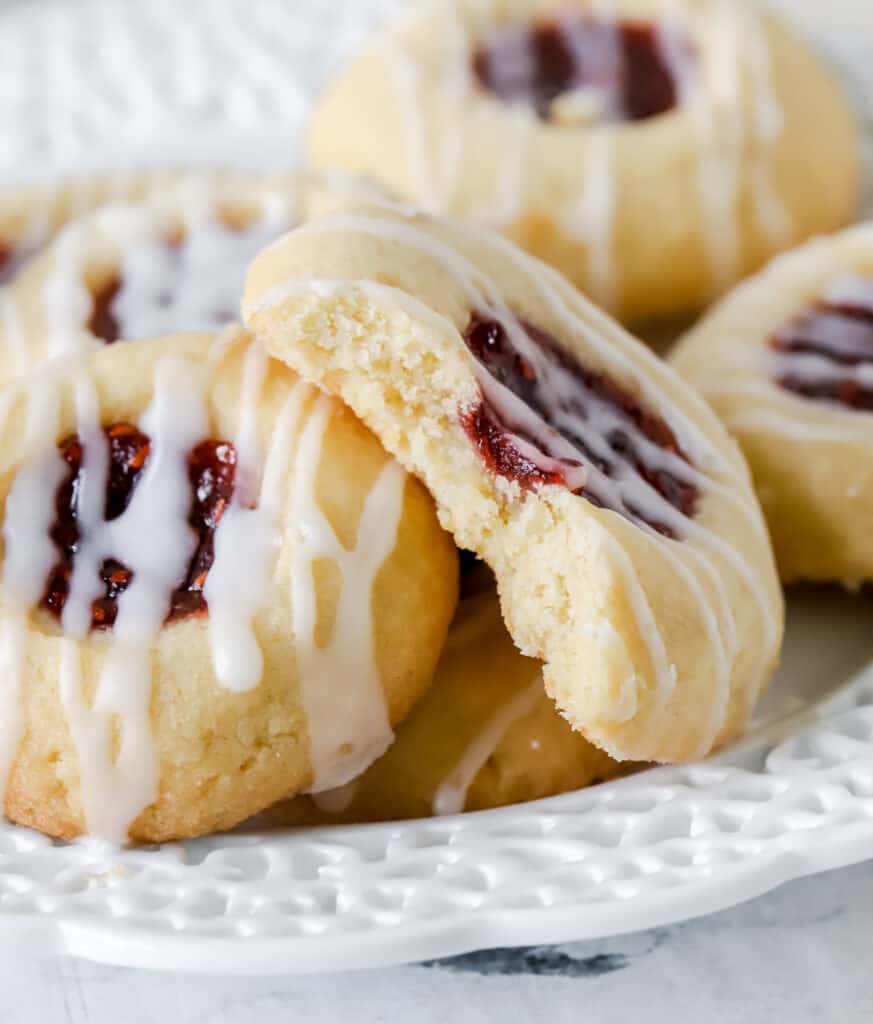 raspberry thumbprint cookies on a plate with a bite missing