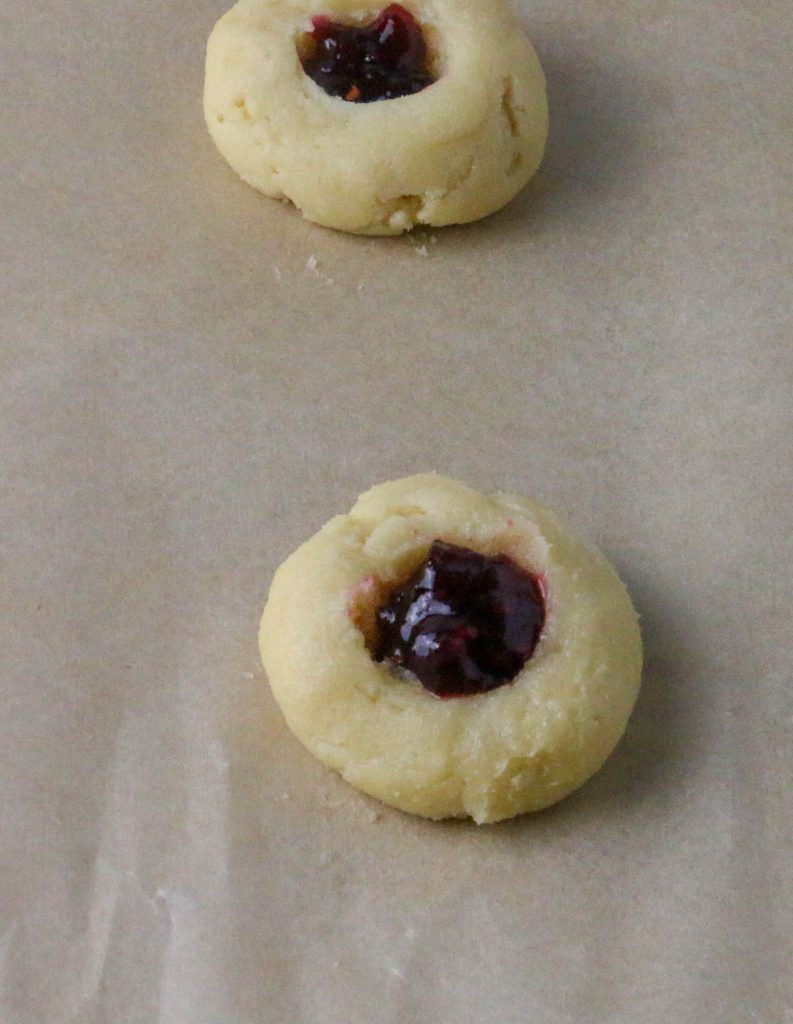raspberry thumbprint cookies unbaked on a cookie sheet