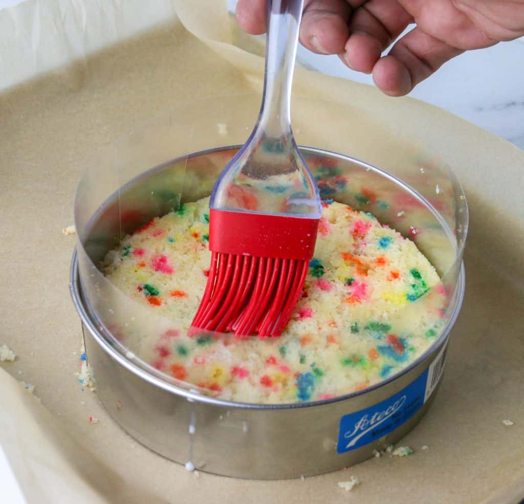 milk soak being spread into cake with red silicone brush