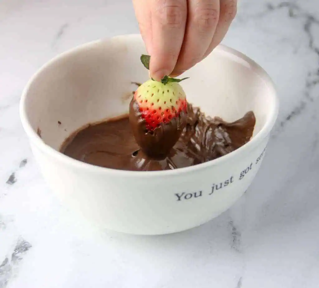 strawberry dipped in bowl of melted chocolate