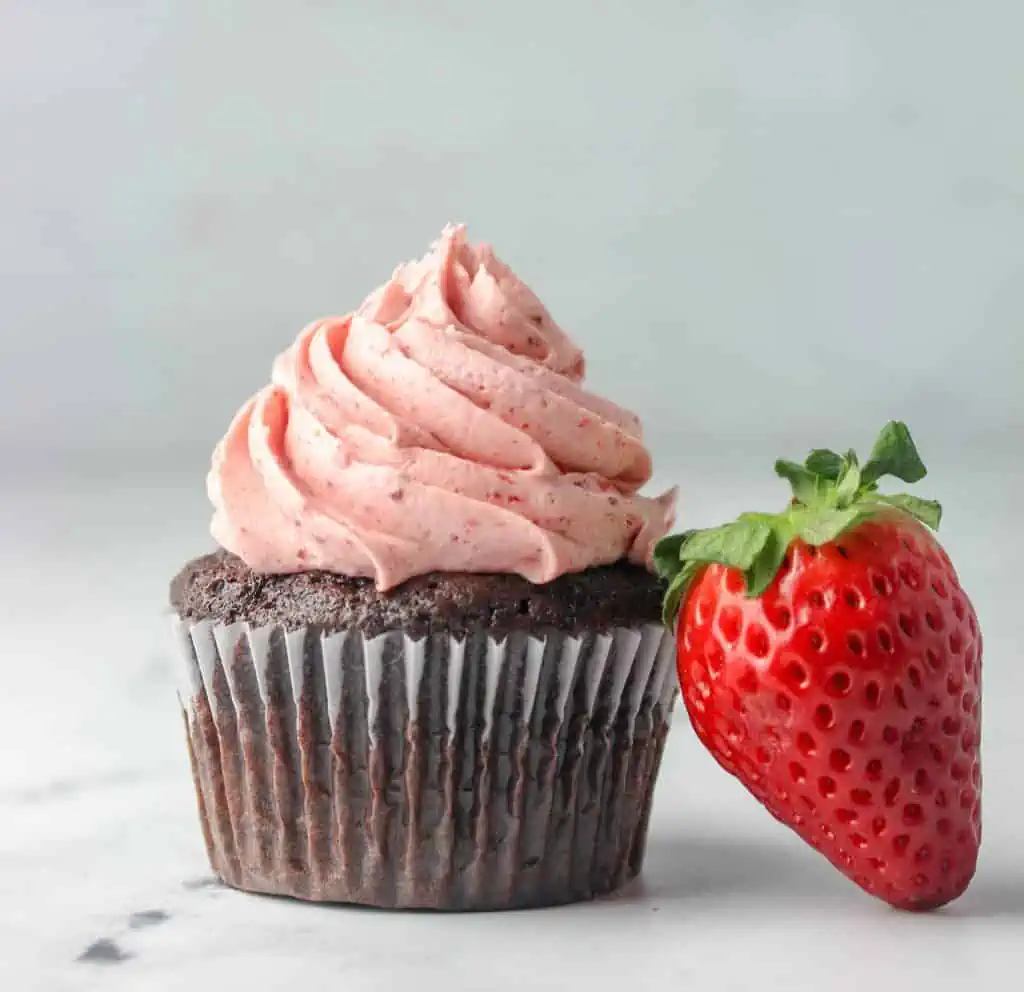 chocolate cupcake with strawberry buttercream and a strawberry next to it