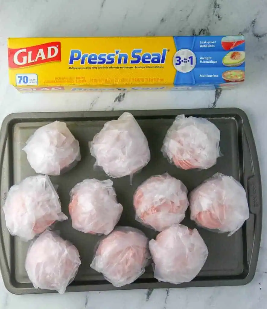 cupcakes wrapped in plastic wrap on a cookie sheet