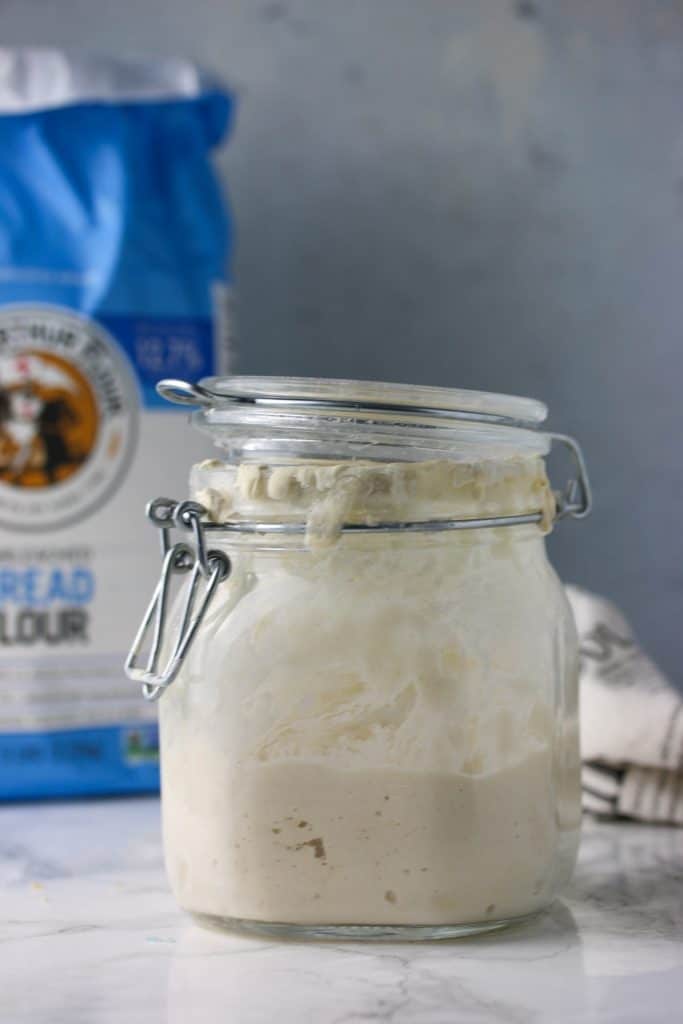 glass jar of sourdough starter and a bag of bread flour
