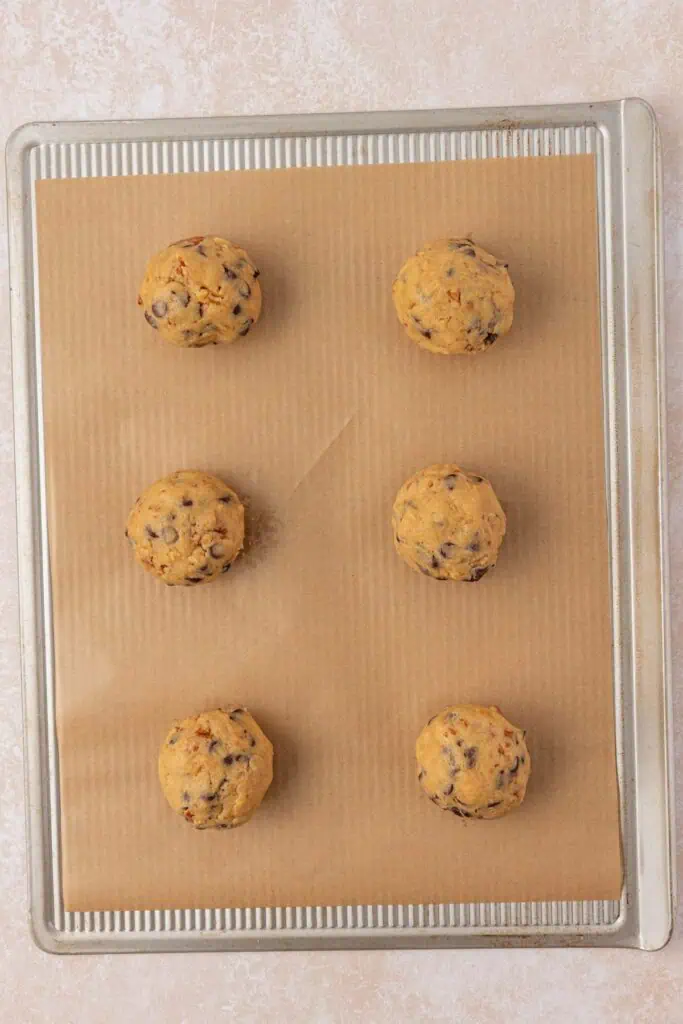 six cookie dough balls on a cookie sheet