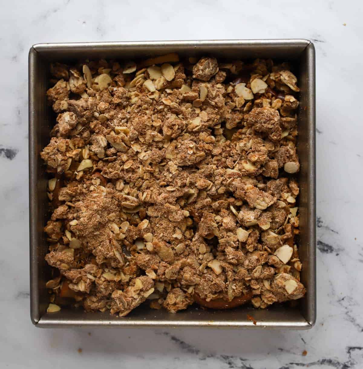 apple crisp topping sprinkled on top off apple mixture in square pan