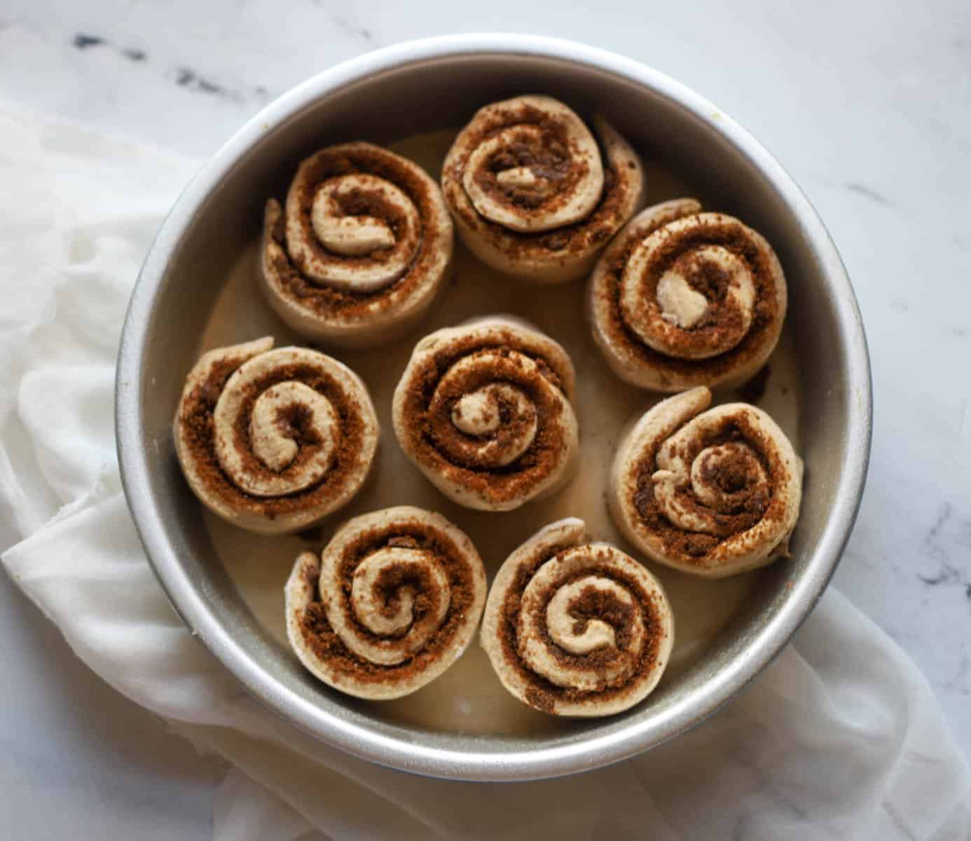 eight cinnamon rolls in a round cake pan unrisen
