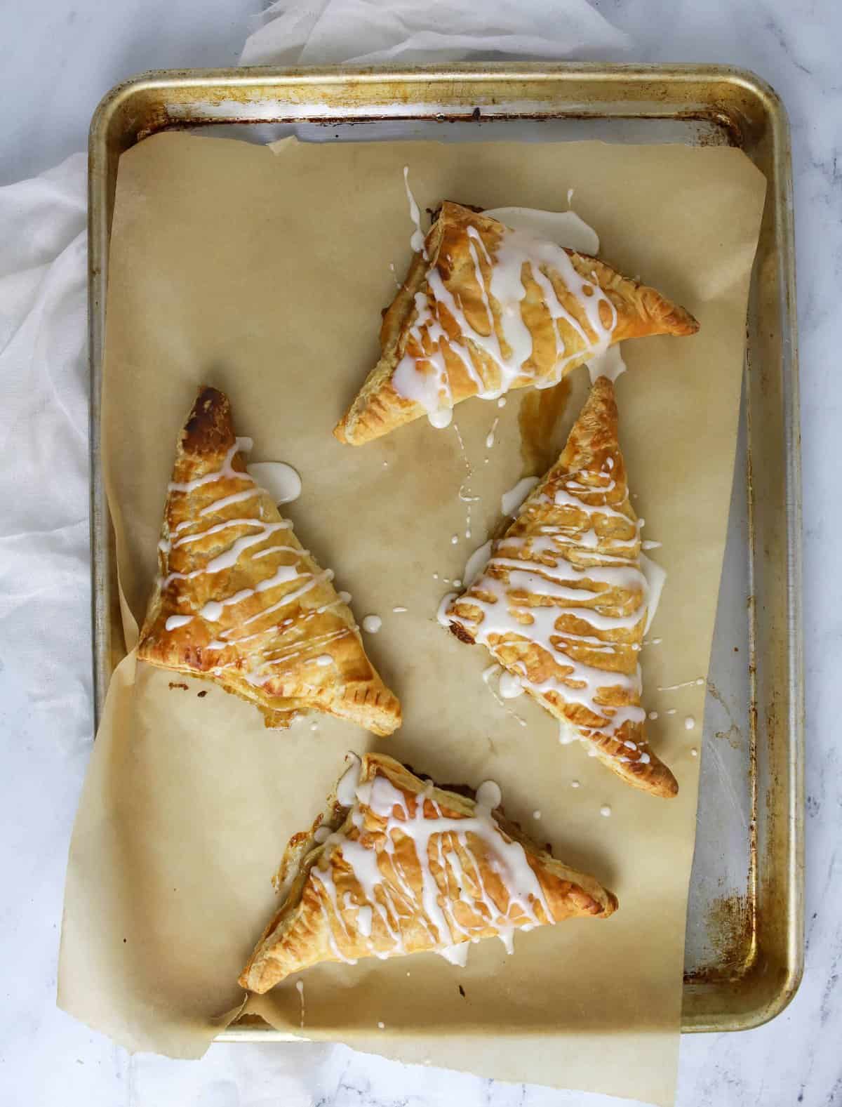 four pear turnovers on a baking sheet with glaze on top