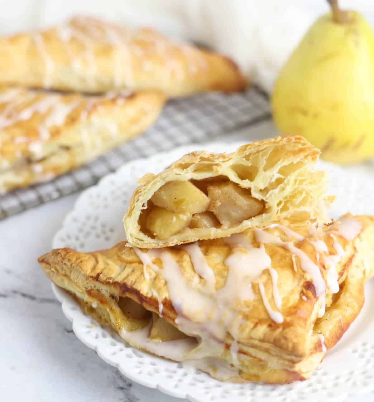 two pear turnovers stacked on a plate, with one cut in half