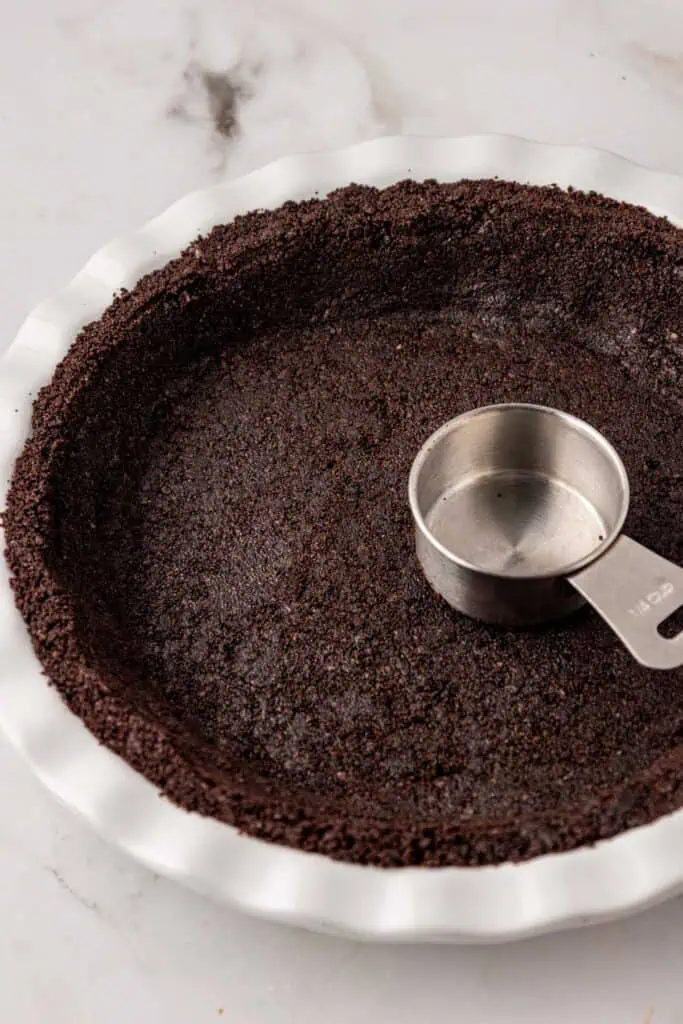 oreo cookie crust pressed down into pie plate with a measuring cup