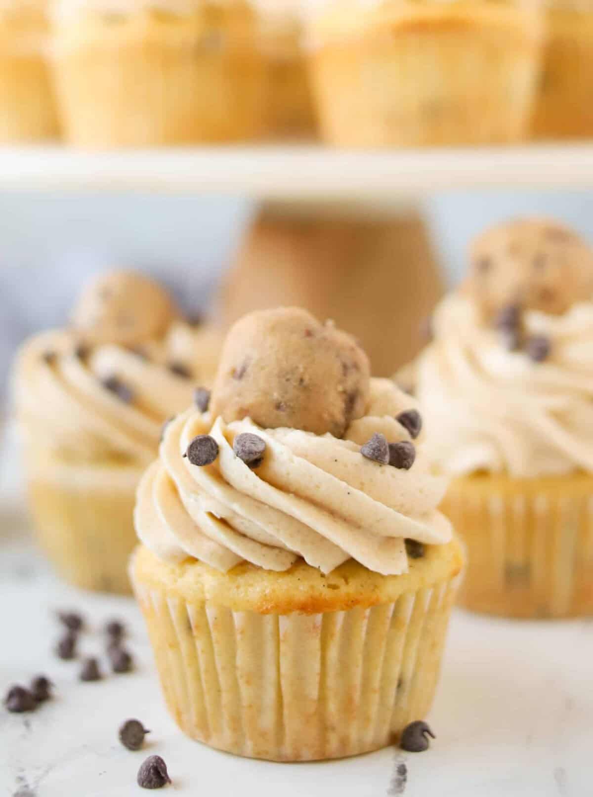 cookie dough cupcake with more cupcakes behind it on a cupcake stand