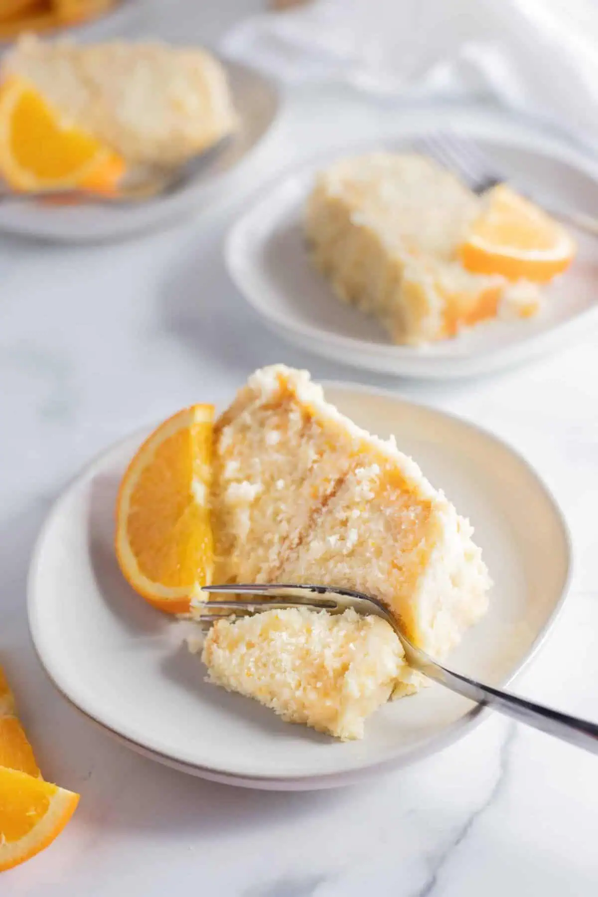 orange creamsicle cake slices on a plate with a fork with an orange slice