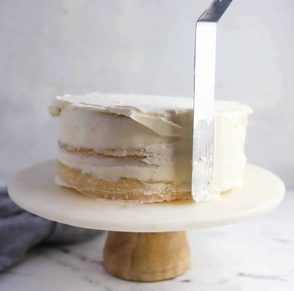 spatula spreading frosting on sides of cake
