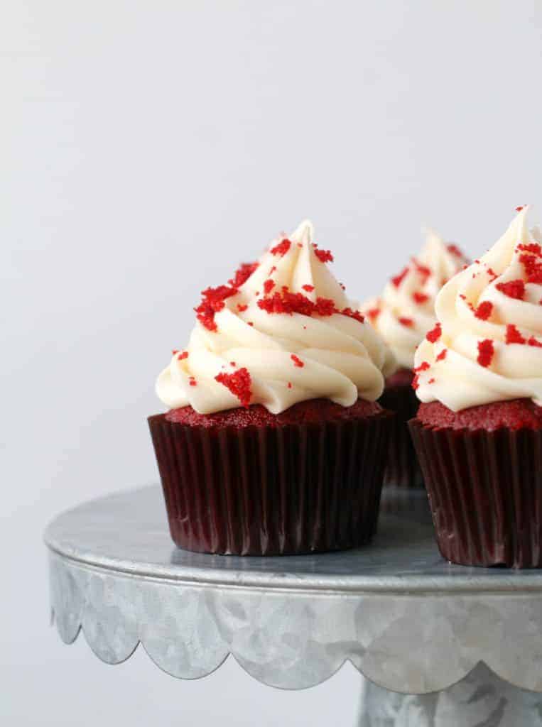 red velvet cupcakes with cream cheese frosting on a metal cake stand