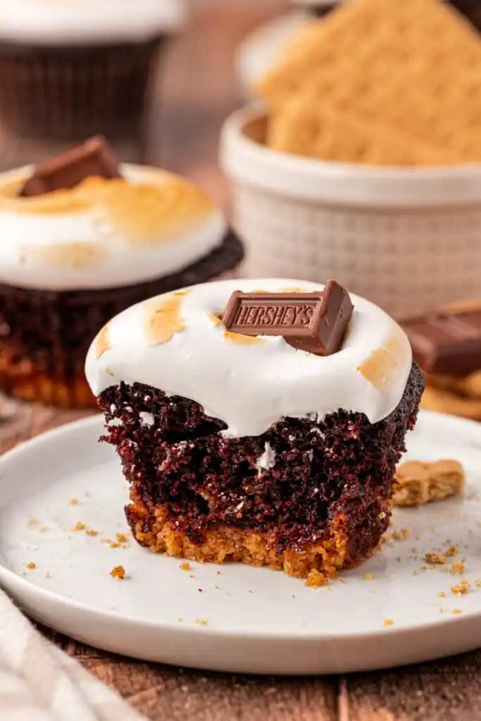 S'mores Cupcakes- chocolate cupcakes with marshmallow frosting and graham cracker bottom! half of a smores cupcake on a plate
