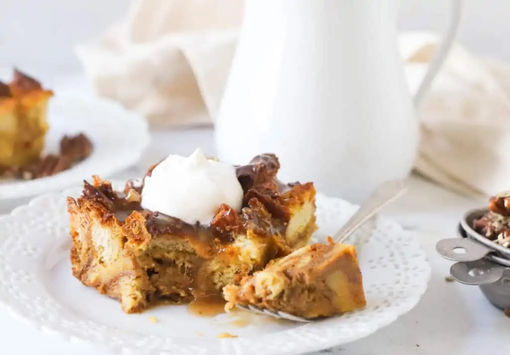 slice of pumpkin bread pudding on a plate with a fork topped with whipped cream