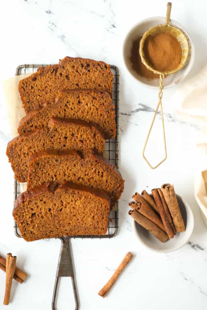 pumpkin bread slices on a wire rack with cinnamon sticks next to it