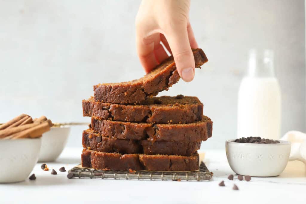 hand remove a slice of chocolate chip pumpkin bread from a stack