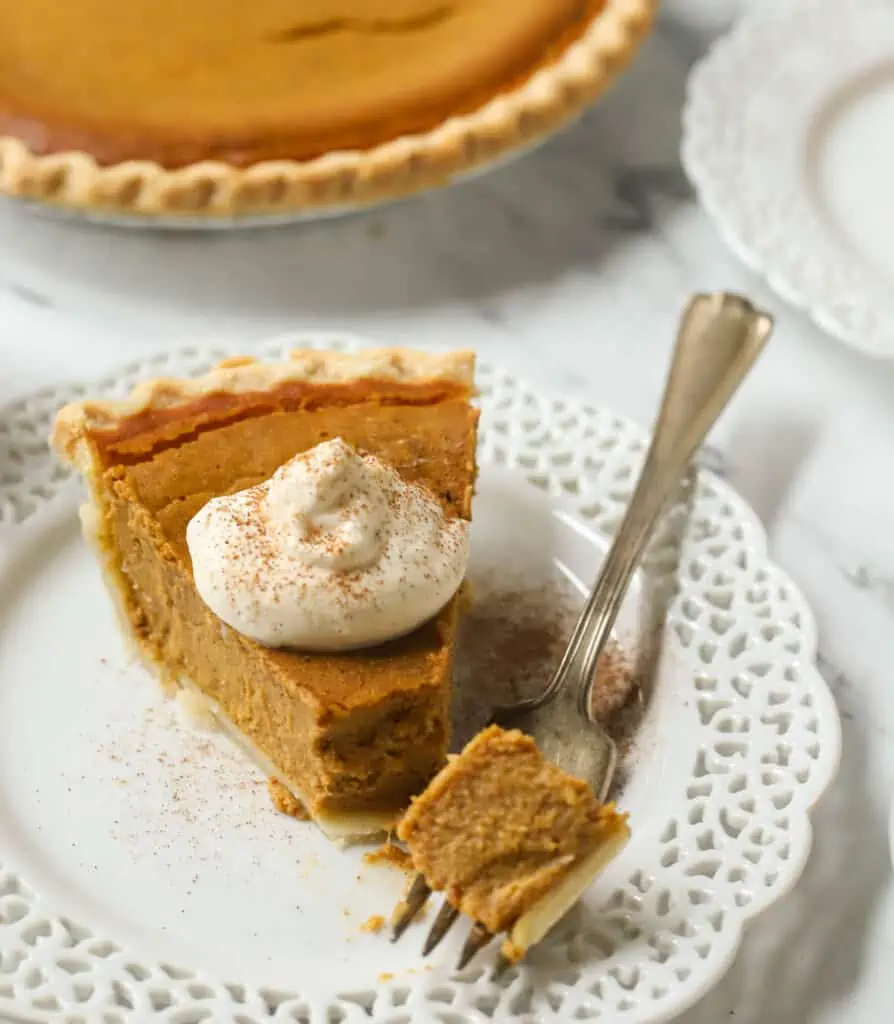 slice of pumpkin pie on a plate with a fork and topped with whipped cream
