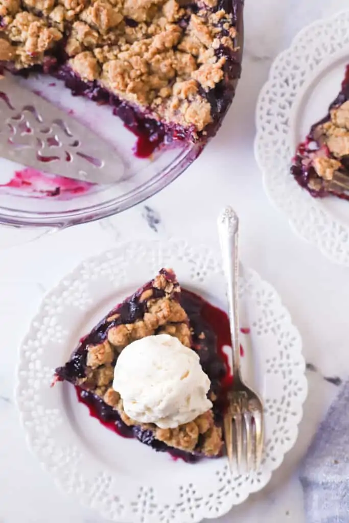 top down view of blueberry crumble pie slice topped with ice cream on a plate with a fork