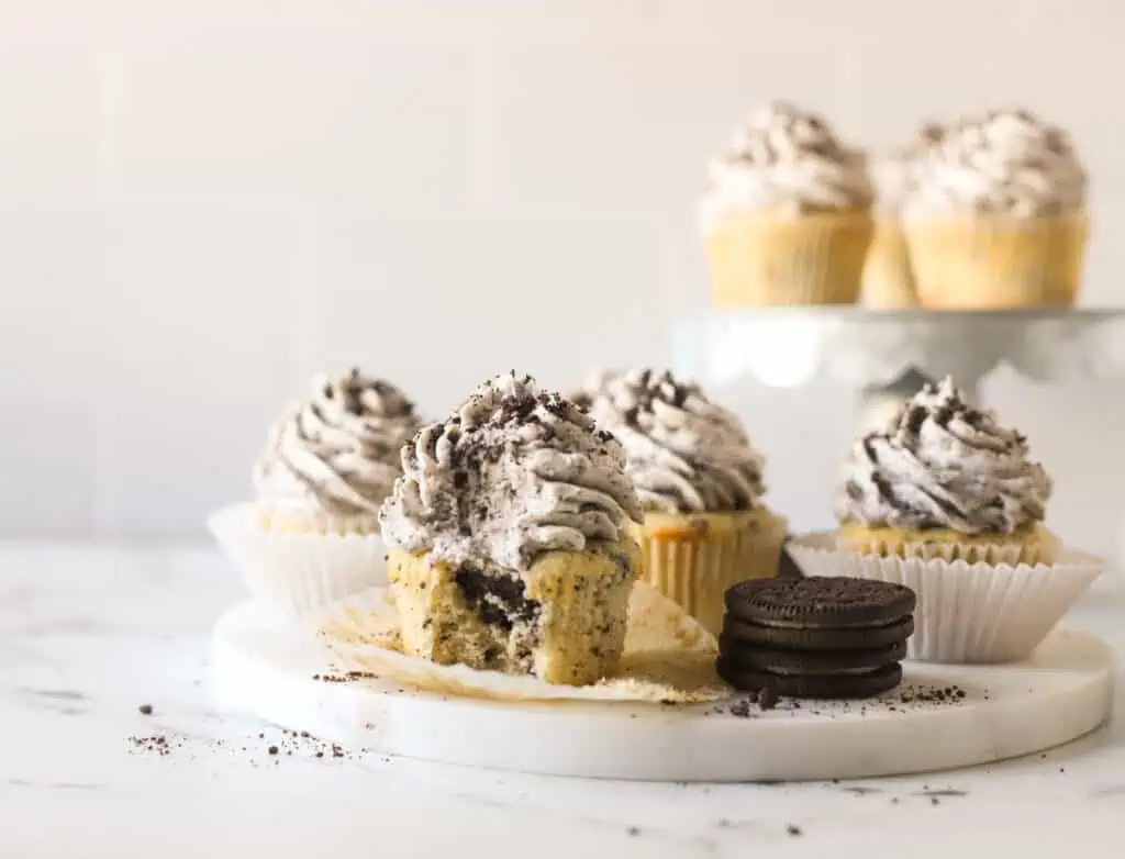 oreo cupcakes on a marble platter, and one cupcake has a bite taken out of it
