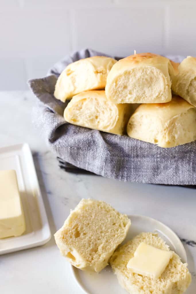 dinner rolls in a basket and one cut open topped with butter on a plate