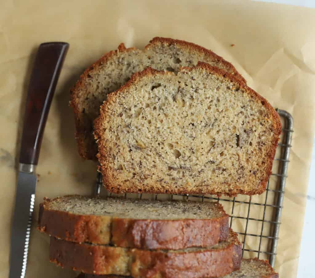two slices of sour cream banana bread on a wire rack with a knife