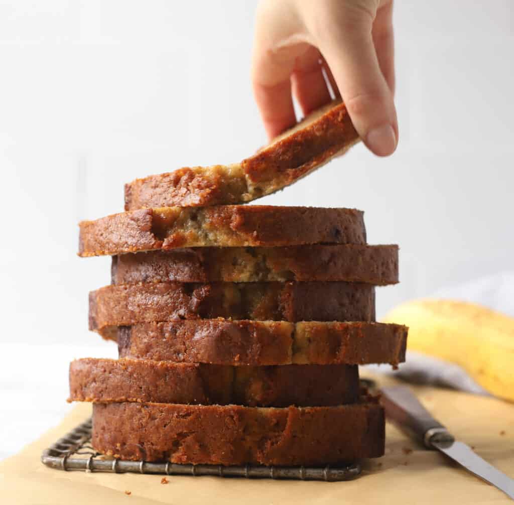 hand holding a slice of banana bread on top of a stack of banana bread