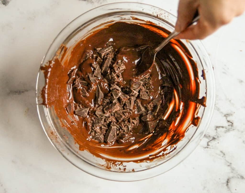 a hand stirring chopped chocolate into melted chocolate