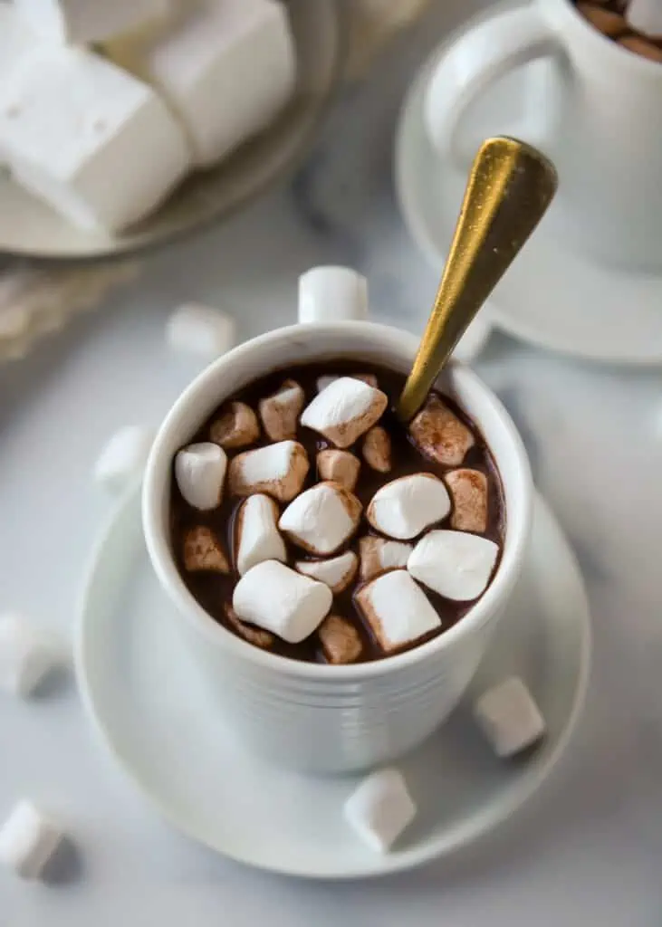 cup of hot cocoa topped with marshmallows with a gold spoon in it