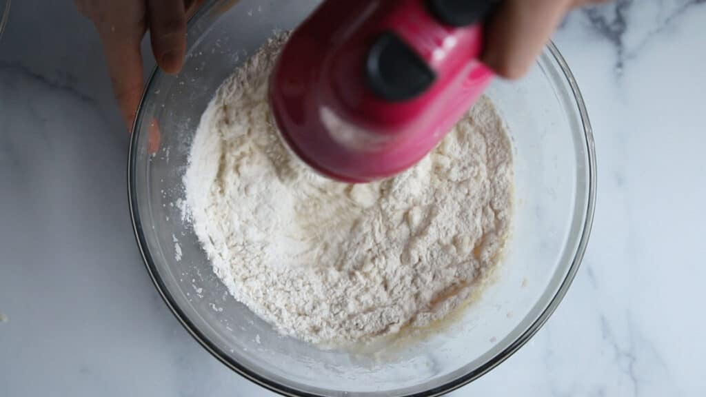 pink hand mixer mixing flour into white cake batter