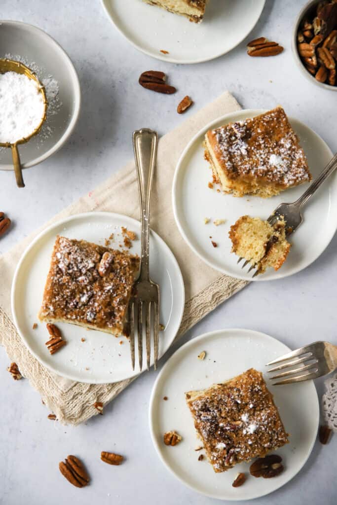three slices of sour cream cinnamon coffee cake on white plates with forks
