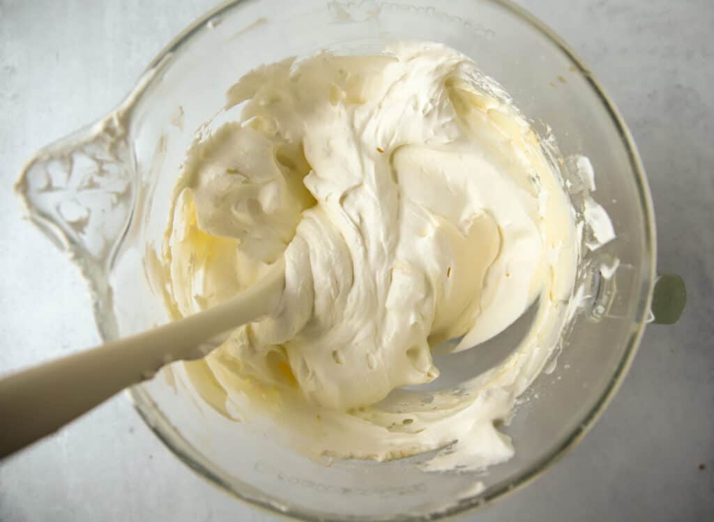 white spatula folding whipped cream into Chantilly cake frosting